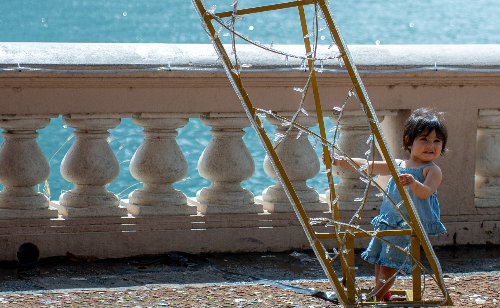 A toddler playing with a light-frame by the sea railing