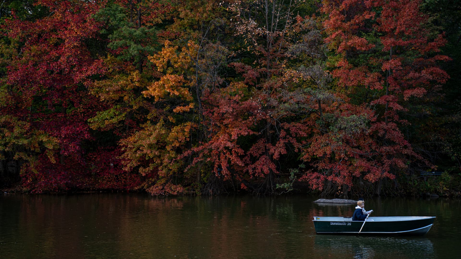 A lone rowboat on a still lake against autumn foliage