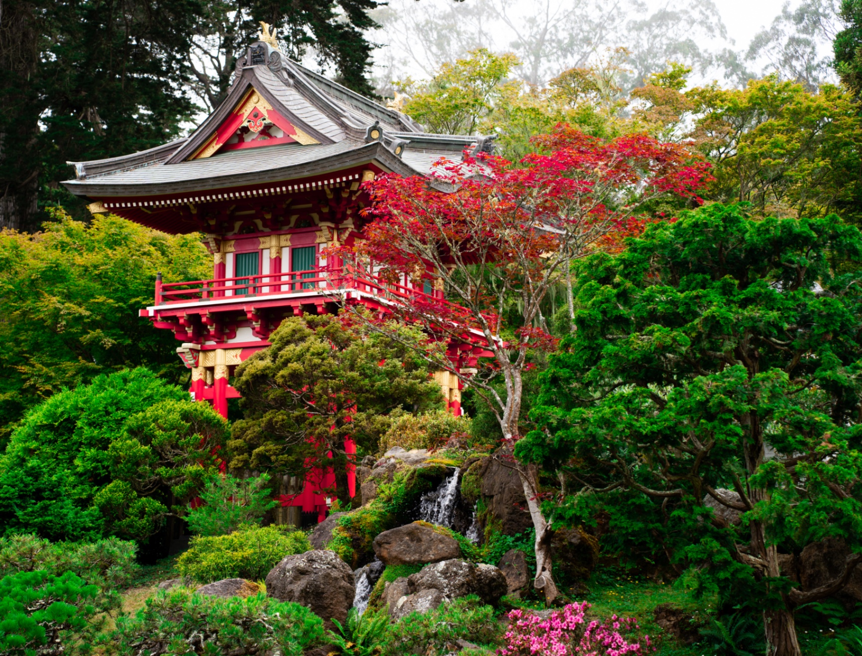 A red Japanese tea house above a waterfall among maples