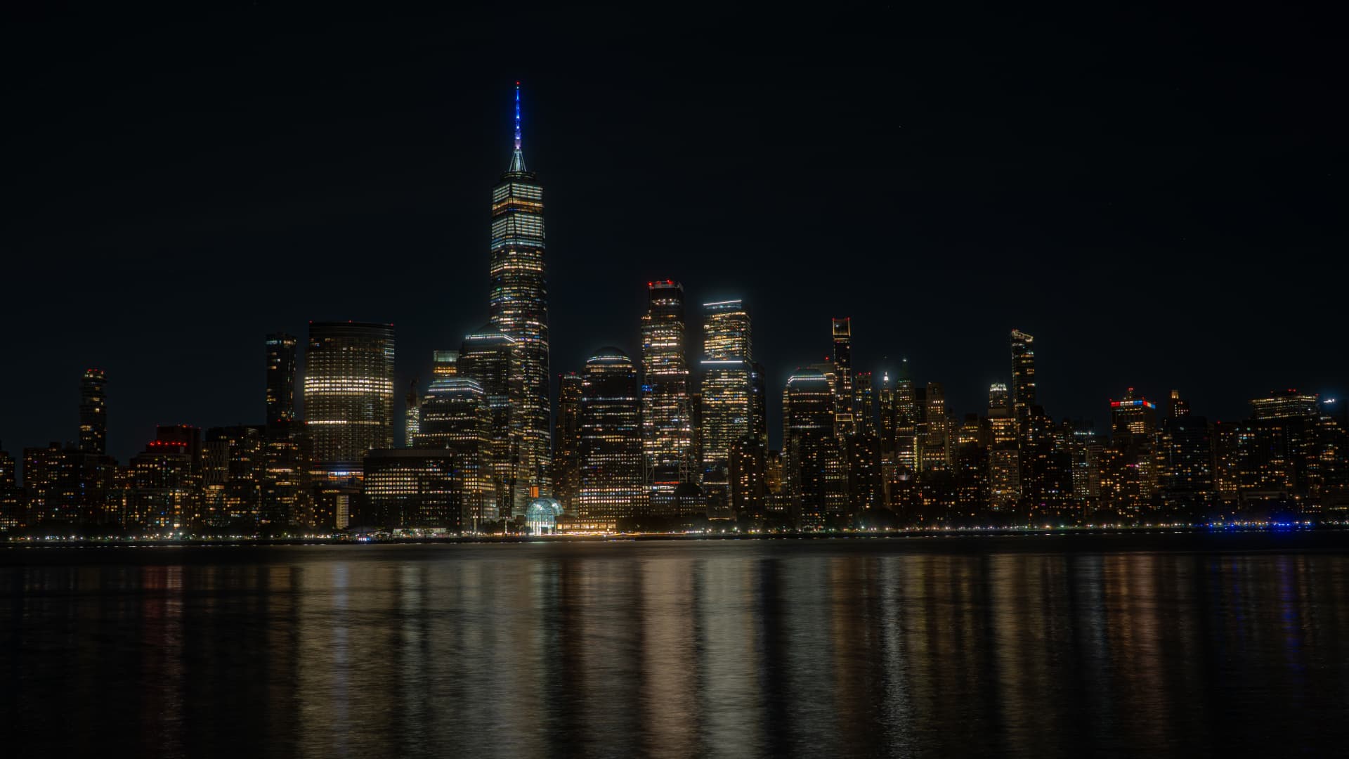 New York City skyline at night, lights reflecting on the water